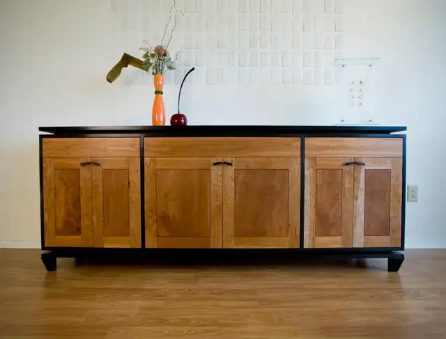Cherry sideboard with three paneled doors set in a black frame on a light wood floor